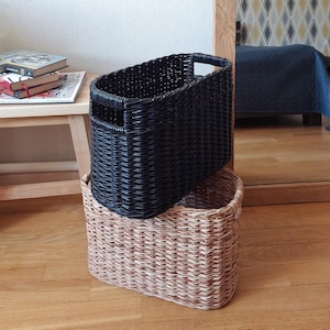 May include: Two woven storage baskets, one black and one natural brown, are stacked on top of each other. The baskets are oval shaped and have a woven pattern.
