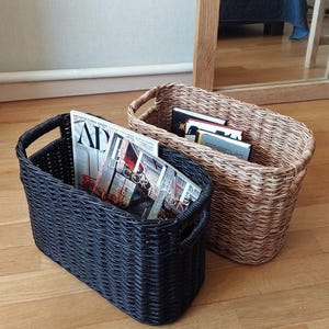May include: Two woven storage baskets, one black and one brown, filled with magazines. The magazines have titles such as "Architectural Digest" and "Decor".
