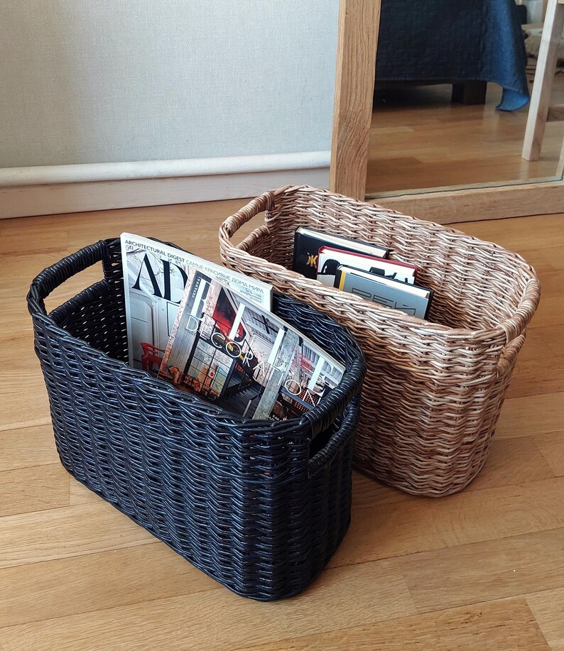 May include: Two woven storage baskets, one black and one brown, filled with magazines. The magazines have titles such as "Architectural Digest" and "Decor".