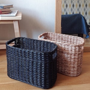 May include: Two woven storage baskets, one black and one natural brown, with handles. The baskets are made of a woven material and have a rectangular shape.