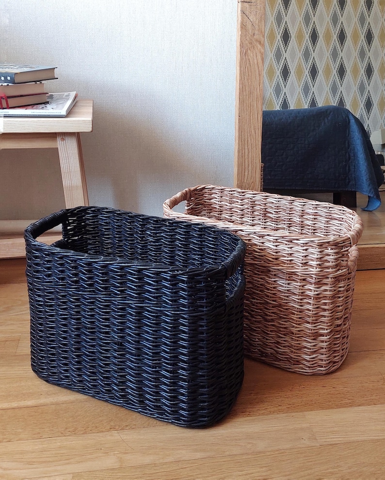 May include: Two woven storage baskets, one black and one natural brown, with handles. The baskets are made of a woven material and have a rectangular shape.