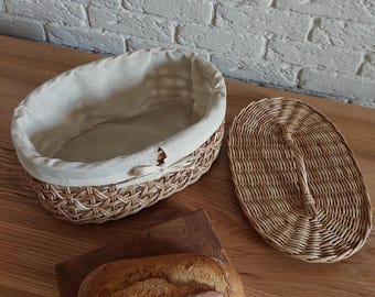 May include: Oval wicker bread basket with a removable lid and a white linen liner. The basket is made of natural woven wicker and has a rustic, farmhouse style.