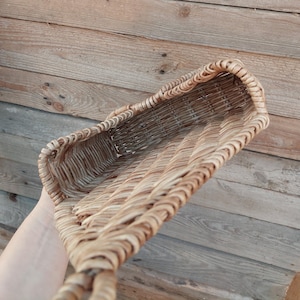May include: A woven wicker basket with a rectangular shape and a handle. The basket is made of natural brown wicker and has a light brown colour.