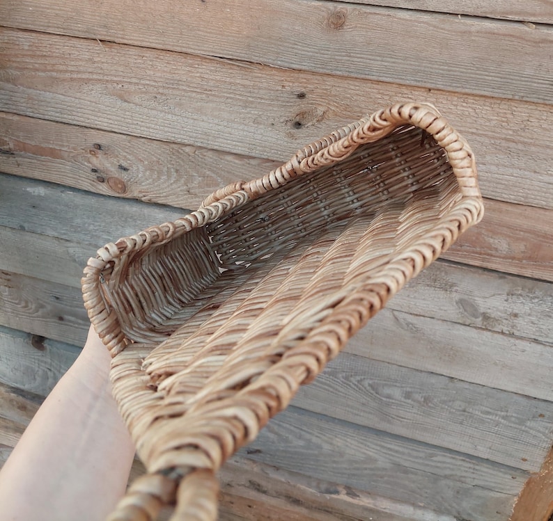 May include: A woven wicker basket with a rectangular shape and a handle. The basket is made of natural brown wicker and has a light brown colour.