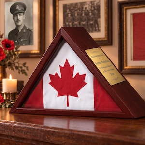 Puede incluir: Una vitrina triangular de madera que contiene una bandera canadiense plegada. Una placa de metal dorado en el marco dice: Presented With Honor to Robert Anderson For Distinguished Service to the United States 2026.