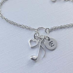 May include: Silver charm bracelet with a heart, music note, and initial E charm. The bracelet has a double chain design.