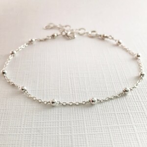 May include: A delicate silver chain bracelet with small round beads. The bracelet is made of a thin chain and has a simple, elegant design.