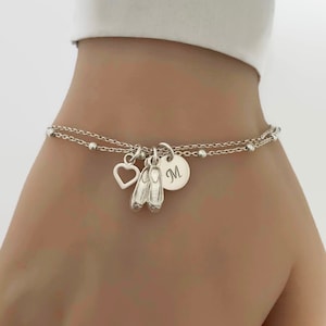 May include: A silver charm bracelet featuring a heart, ballet shoes, and a round charm engraved with the letter "M".