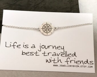 May include: A silver bracelet featuring a compass charm and the inscription "Life is a journey best travelled with friends" on a white card. The card also includes the website "www.jewellerybyzm.etsy.com".