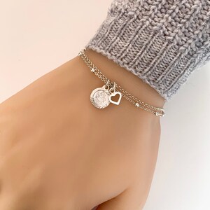 May include: Silver chain bracelet with a small heart charm and a round charm with a detailed design.