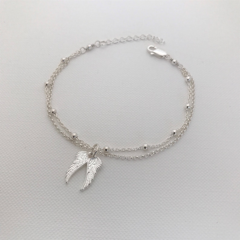 May include: A silver chain bracelet with two strands and a small angel wing charm.