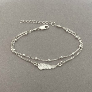 Puede incluir: Un brazalete de cadena de plata con un delicado dije de ala de &aacute;ngel y peque&ntilde;as cuentas. El brazalete tiene un cierre ajustable.