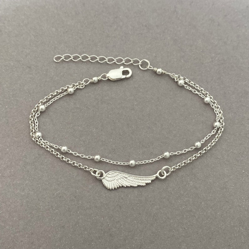 Puede incluir: Un brazalete de cadena de plata con un delicado dije de ala de &aacute;ngel y peque&ntilde;as cuentas. El brazalete tiene un cierre ajustable.