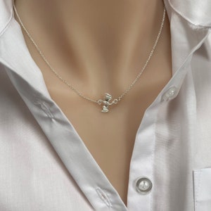 May include: A silver necklace with a small, detailed bat pendant. The necklace is on a model wearing a white shirt.