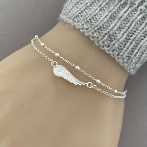 Puede incluir: Un brazalete de cadena de plata con un delicado dije de ala de &aacute;ngel y peque&ntilde;as cuentas de plata. El brazalete est&aacute; formado por dos cadenas superpuestas.