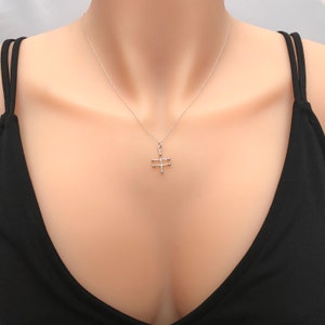 May include: A silver necklace with a geometric pendant featuring a cross design with small circles at the ends of each line.