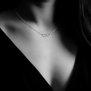 May include: A silver infinity necklace worn on a person's neck. The necklace features a simple design with a fine chain.