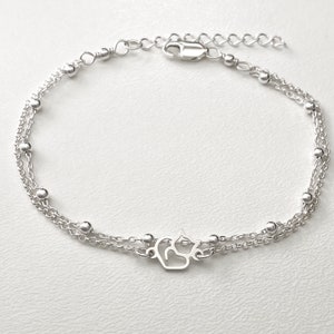 May include: A silver chain bracelet with a delicate cat charm. The bracelet has two strands of chain with small silver beads.