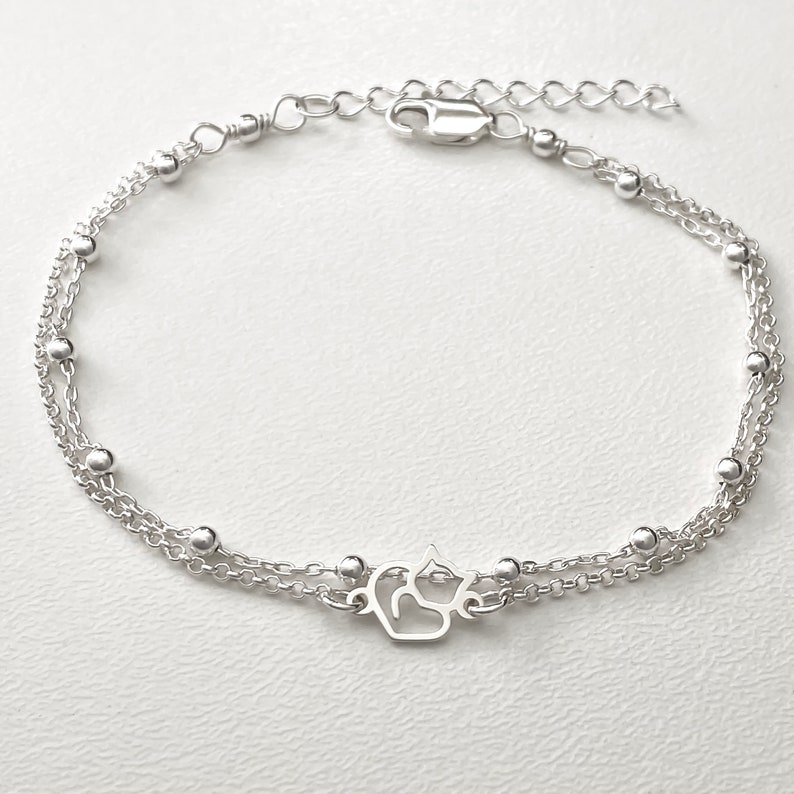 May include: A silver chain bracelet with a delicate cat charm. The bracelet has two strands of chain with small silver beads.