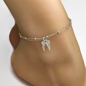 May include: Silver ankle bracelet with two chains and a small angel wing charm.