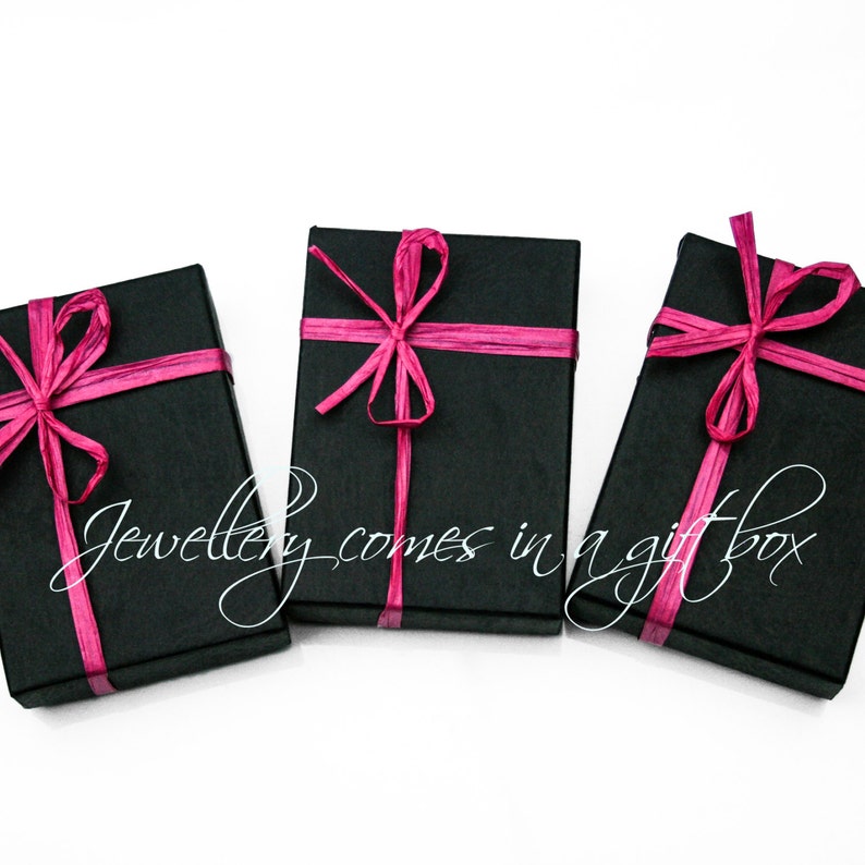 May include: Three black gift boxes with pink ribbon bows. The boxes are on a white background.  "Jewellery comes in a gift box" is written in white cursive on the image.