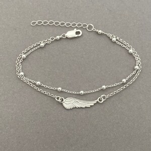 Puede incluir: Un brazalete de cadena de plata con un delicado dije de ala. El brazalete tiene un dise&ntilde;o de cadena doble con peque&ntilde;as cuentas.
