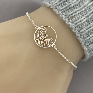 May include: A silver bracelet with a circular pendant featuring a detailed cutout design of a wave.