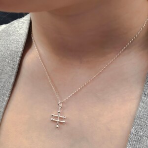 May include: A silver chain necklace with a geometric pendant featuring a stylized cross design with round accents.