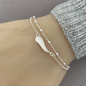 Puede incluir: Un brazalete de cadena de plata con un delicado dije de ala de &aacute;ngel. El brazalete est&aacute; formado por una segunda cadena con peque&ntilde;as cuentas de plata.