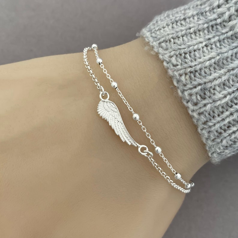 Puede incluir: Un brazalete de cadena de plata con un delicado dije de ala de &aacute;ngel. El brazalete est&aacute; formado por una segunda cadena con peque&ntilde;as cuentas de plata.