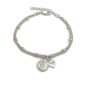May include: A silver chain bracelet with a delicate heart charm and a round charm featuring a religious figure. The bracelet has a lobster clasp closure.