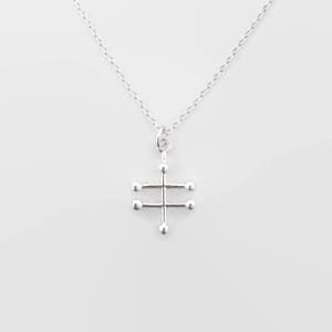 May include: A silver necklace with a geometric pendant featuring a cross shape with small circles at the ends of each arm.