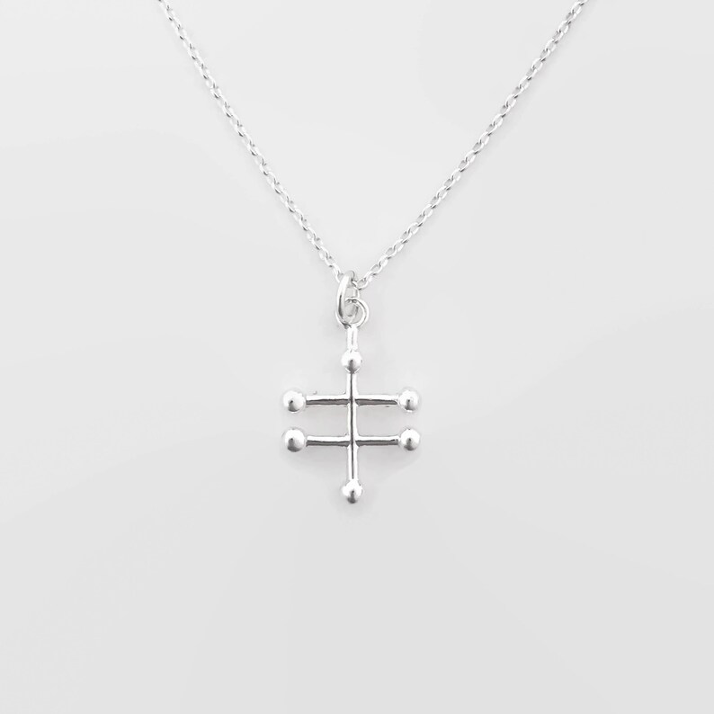 May include: A silver necklace with a geometric pendant featuring a cross shape with small circles at the ends of each arm.