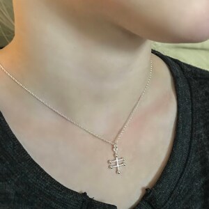 May include: A silver chain necklace with a geometric pendant. The pendant is made of small silver balls connected by thin silver bars.