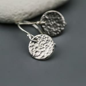 May include: A pair of silver earrings with a hammered texture. The earrings are round and have a simple design.