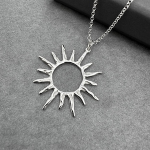 May include: A silver necklace with a sun pendant. The pendant is a circle with rays coming out of it.