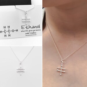 May include: A silver necklace with a pendant shaped like the chemical structure of ethanol. The pendant is on a silver chain. The necklace is displayed on a white card with the text "Ethanol" and the phrase "when life gives you lemons add Vodka".
