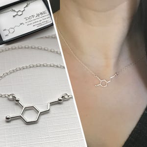 以下が含まれることがあります： ドーパミンの化学構造の形をしたペンダントが付いたシルバーネックレス。ネックレスは白い背景にあり、ペンダントはピントが合っています。カードのテキストには、「ドーパミンは、愛の神経伝達物質であり、幸せを感じさせ、幸せなことをさせます。」と書いてあります。