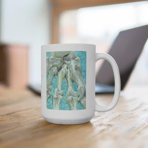 May include: White ceramic mug with a detailed illustration of a hand's skeletal structure. The artwork is set against a light blue background. The mug has a large handle and a glossy finish, suitable for hot drinks.
