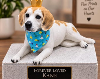 May include: A beagle figurine wearing a gold crown and a blue bandana with a colorful party hat pattern. The dog rests on a rectangular gray granite-style base featuring a black plaque with the gold text "FOREVER LOVED KANE" engraved on it.