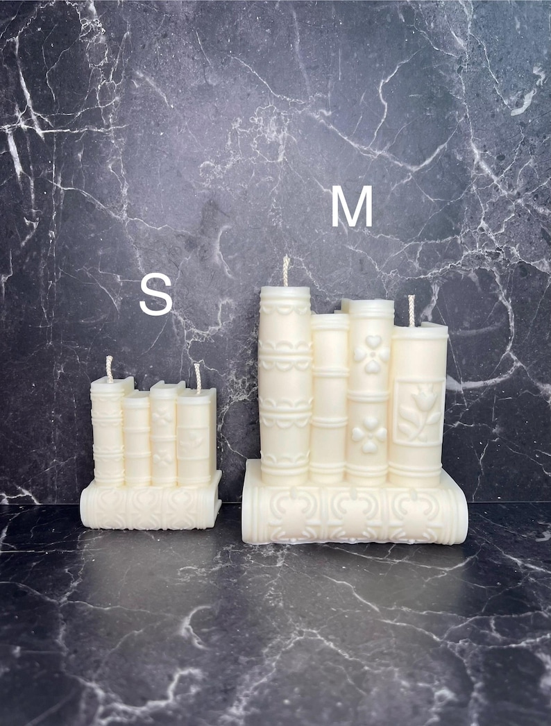 May include: Two white candle sets shaped like stacks of books. The smaller set is labelled "S" and the larger set is labelled "M".