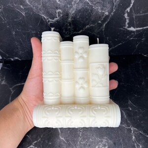 May include: A white pillar candle set with intricate floral designs. The candles are arranged in a row and have a decorative base.