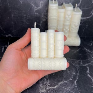 May include: A set of five white candle books with decorative designs. The candles are arranged in a stack, with the largest candle at the bottom and the smallest candle at the top.