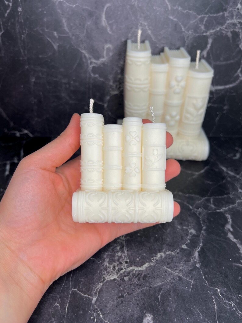 May include: A set of five white candle books with decorative designs. The candles are arranged in a stack, with the largest candle at the bottom and the smallest candle at the top.