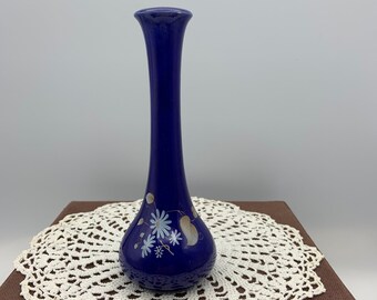 Puede incluir: Un pequeño jarrón de cerámica azul cobalto con un diseño floral blanco. El jarrón tiene un cuello estrecho y una base redondeada.