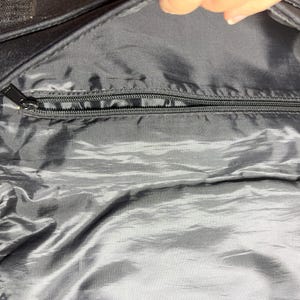 May include: Black bag interior with a silver-colored, shiny lining. A black zipper runs across the top, with a black zipper pull. The bag's exterior is black, and the image is taken from an overhead perspective.