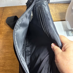 May include: Black messenger bag with a long adjustable strap. The bag has a zippered pocket and a main compartment. The interior lining is black. The bag is made of a durable, water-resistant material.