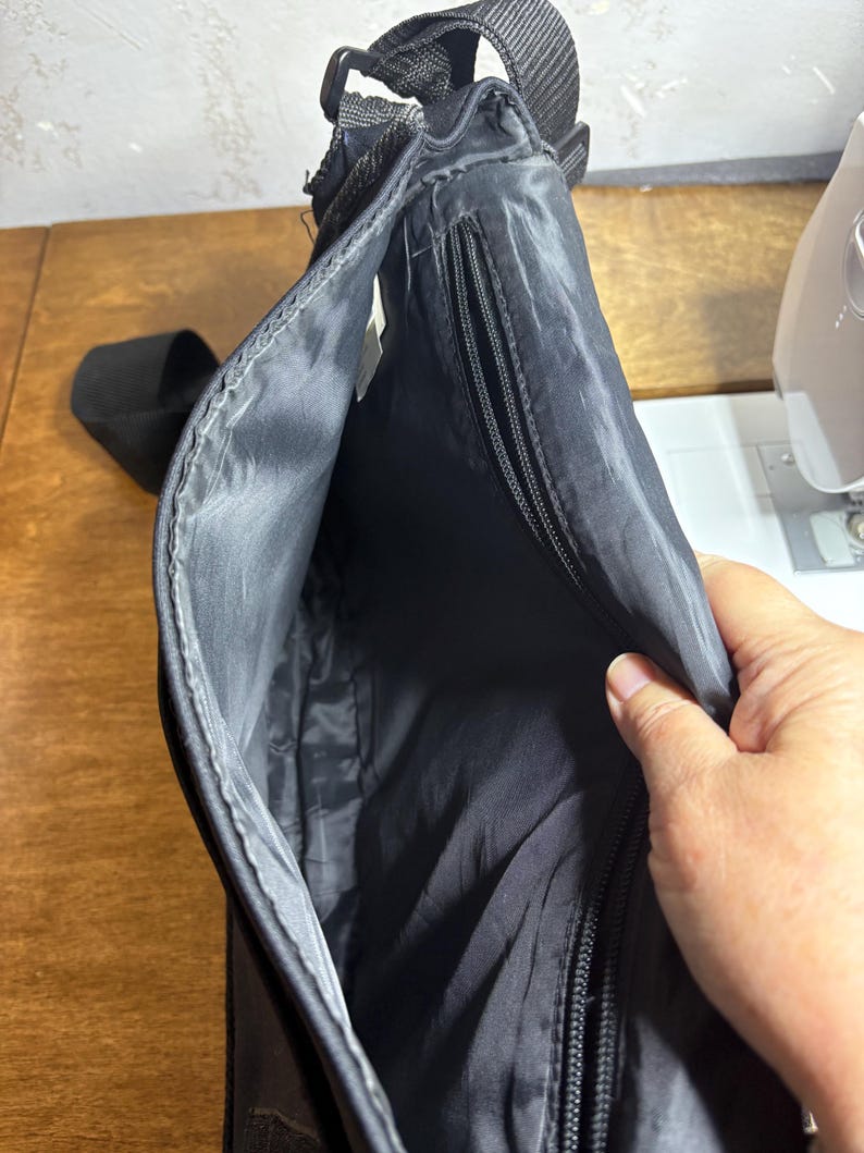 May include: Black messenger bag with a long adjustable strap. The bag has a zippered pocket and a main compartment. The interior lining is black. The bag is made of a durable, water-resistant material.