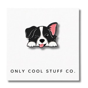 Peut inclure: Un chien border collie noir et blanc avec une oreille rose qui dépasse d'une surface blanche. Le chien fait un clin d'œil et sort sa langue. Le texte "ONLY COOL STUFF CO." est imprimé sous le chien.
