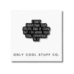 Può includere: Una spilla nera con la scritta "I DON'T UNDERSTAND YOUR SPECIFIC KIND OF STUPID BUT I DO ADMIRE YOUR TOTAL COMMITMENT TO IT." La spilla è su una carta bianca con "ONLY COOL STUFF CO." stampato sotto.